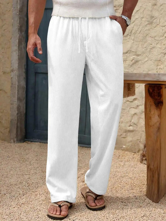 White ribbed knit wide-leg drawstring pants worn by a model, paired with brown sandals, standing in front of a rustic stone wall and wooden bench.