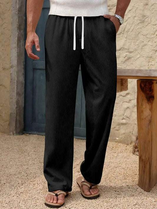A person wearing black ribbed drawstring pants with a white drawstring, standing outdoors next to a wooden bench on a sandy surface.
