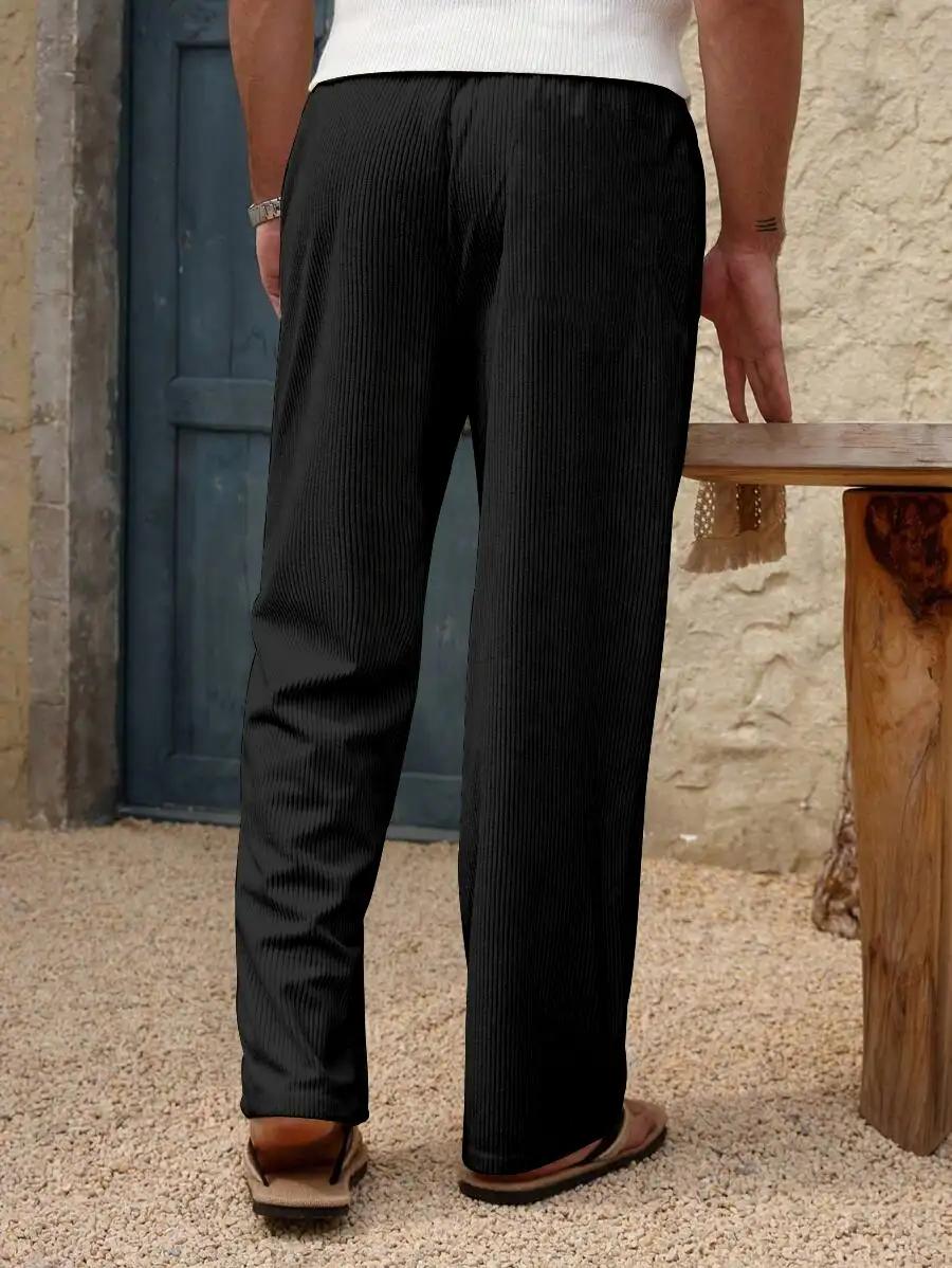 A person viewed from behind wearing black pinstriped trousers, a white top, and brown sandals, standing in a rustic outdoor setting with a wooden bench and textured wall.