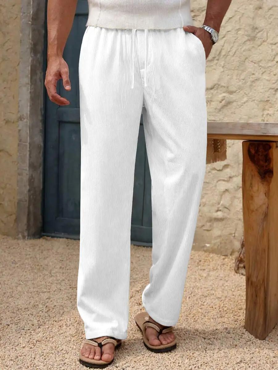 White ribbed knit wide-leg drawstring pants worn by a model, paired with brown sandals, standing in front of a rustic stone wall and wooden bench.