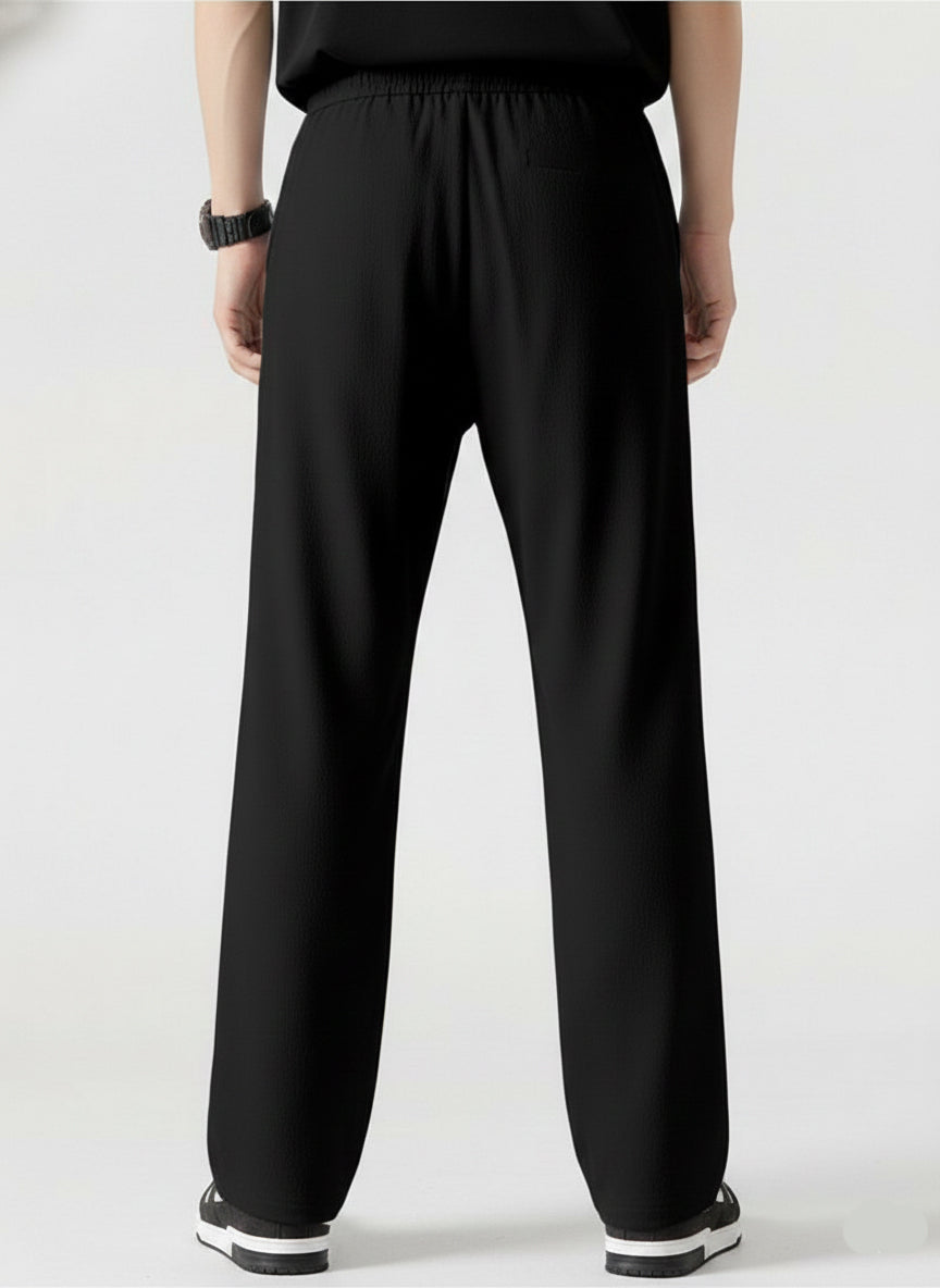 A person shown from the back wearing loose black wide-leg pants, a black top, and black-and-white sneakers against a clean light gray studio background.