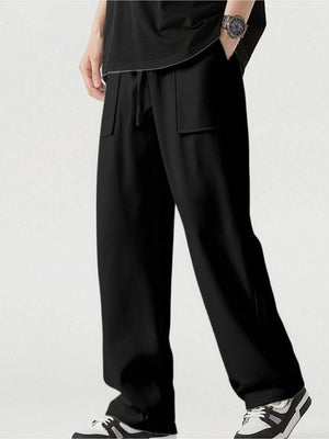 A person wearing loose black wide-leg pants with a drawstring waist and large front patch pockets, paired with a black top and black-and-white sneakers against a light gray studio background.