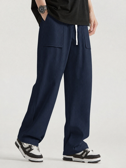 A person wearing loose, wide-leg navy pants with a white drawstring, paired with a black t-shirt and black-and-white sneakers, photographed against a light gray studio background.