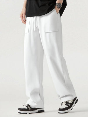 White wide-leg sweatpants with a drawstring waist and large front patch pockets, shown on a model wearing a black t-shirt and black-and-white sneakers against a light gray studio background.
