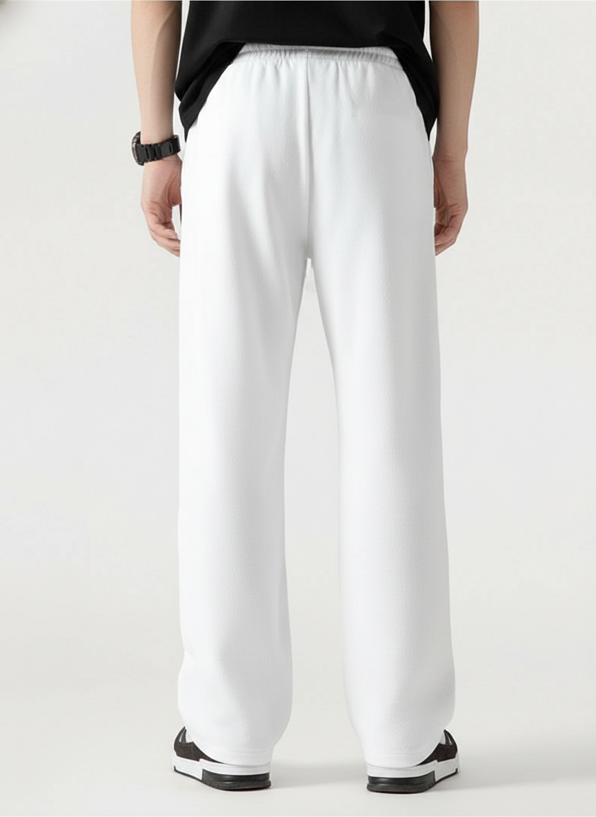White wide-leg sweatpants shown from the back on a model, paired with a black t-shirt and black-and-white sneakers against a light gray studio background.
