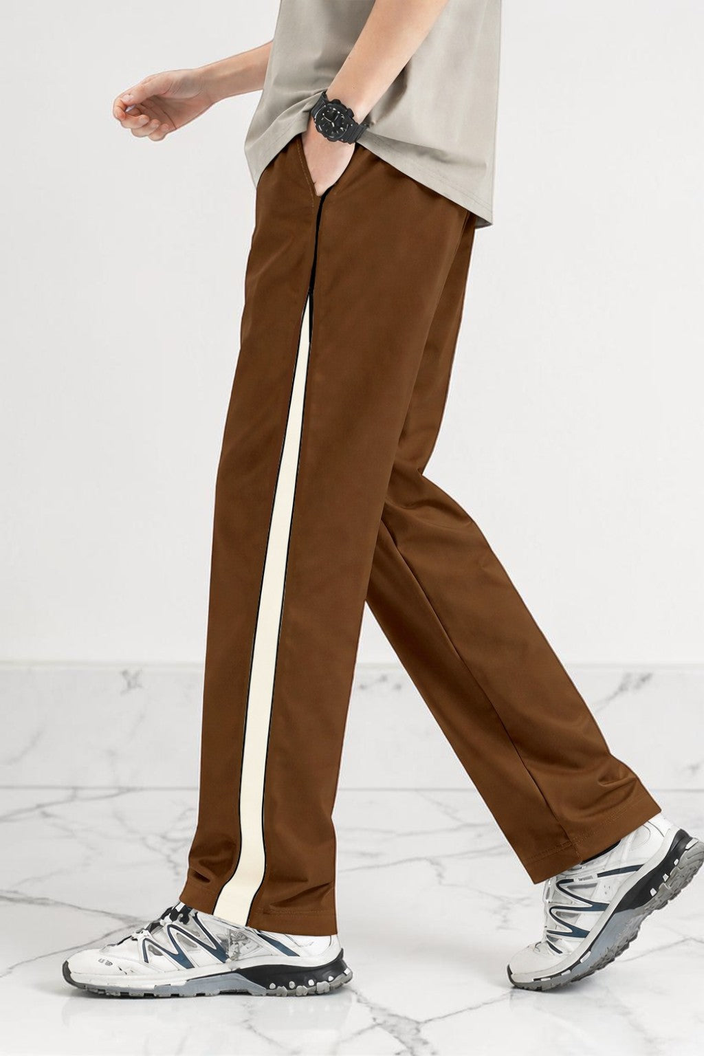 A person wearing coffee wide-leg pants with a vertical cream stripe down the side, paired with a light gray top and white sneakers, shown from the waist down against a clean studio background.