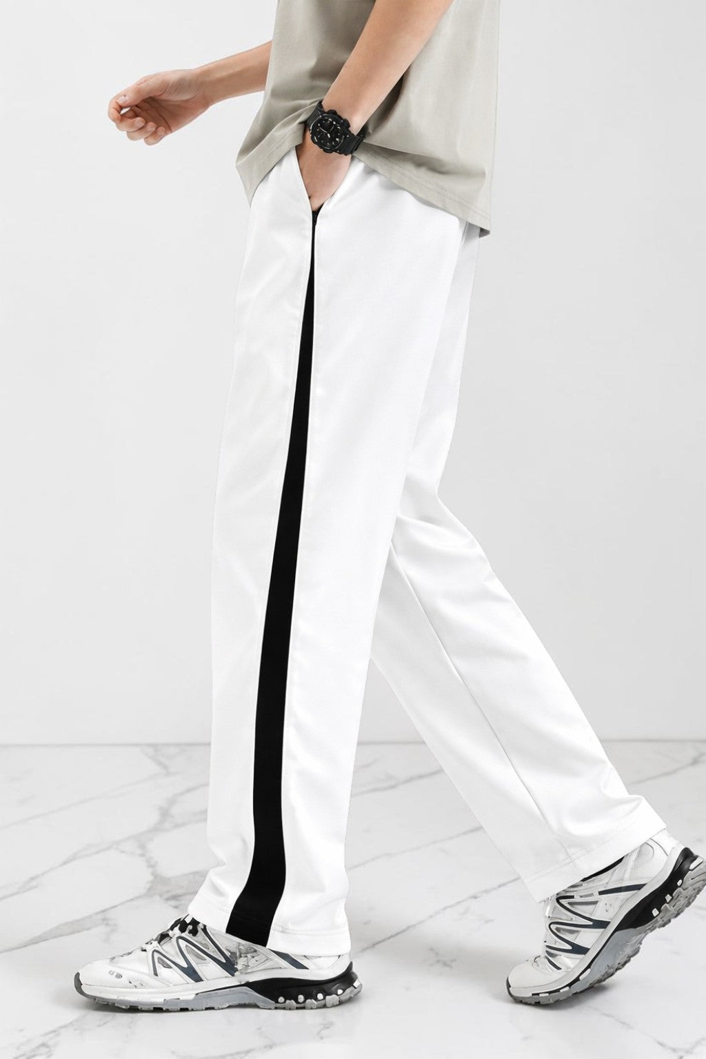 White athletic pants with a bold black side stripe, modeled with a light gray t-shirt and white sneakers on a light gray marble floor.