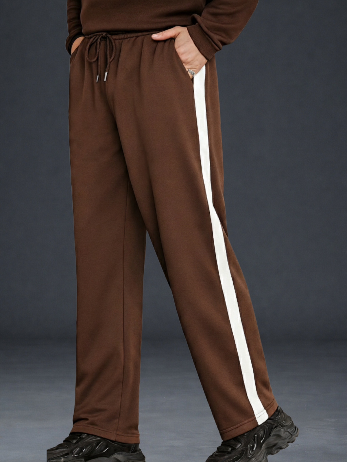 Coffee wide-leg sweatpants with a cream side stripe, shown on a model wearing a matching brown top and black sneakers against a dark gray studio background.