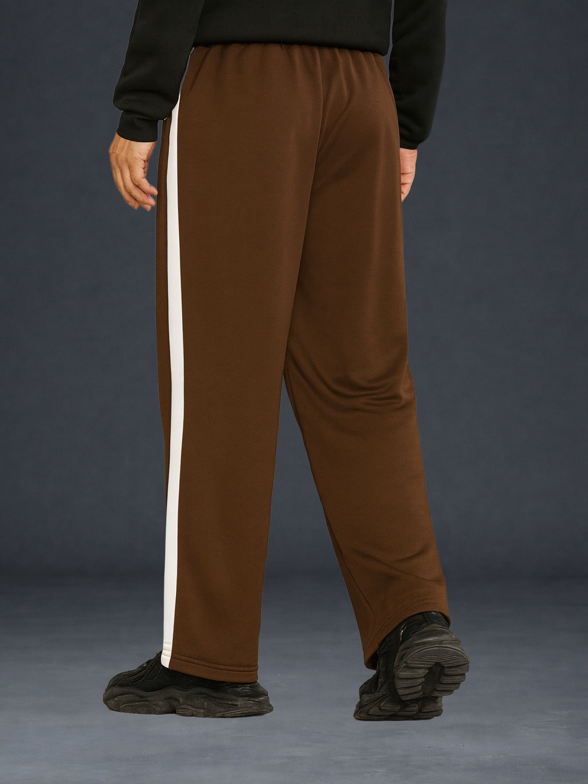 Coffee wide-leg sweatpants with a vertical cream stripe down the side, shown on a model from the back against a dark gray studio background.