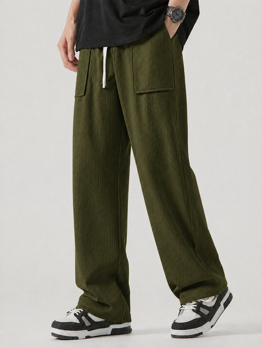 A person wearing olive green corduroy wide-leg pants with a white drawstring, paired with a black t-shirt and black-and-white sneakers, shown from the waist down against a light gray studio background.